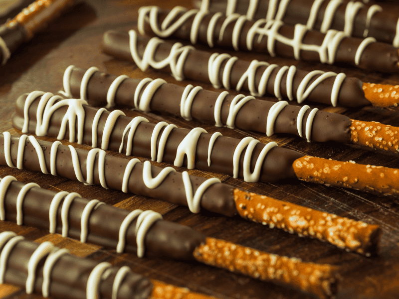 Chocolate-dipped pretzel rods wrapped in clear bags with decorative ties, a fun and tasty baby shower party favor.