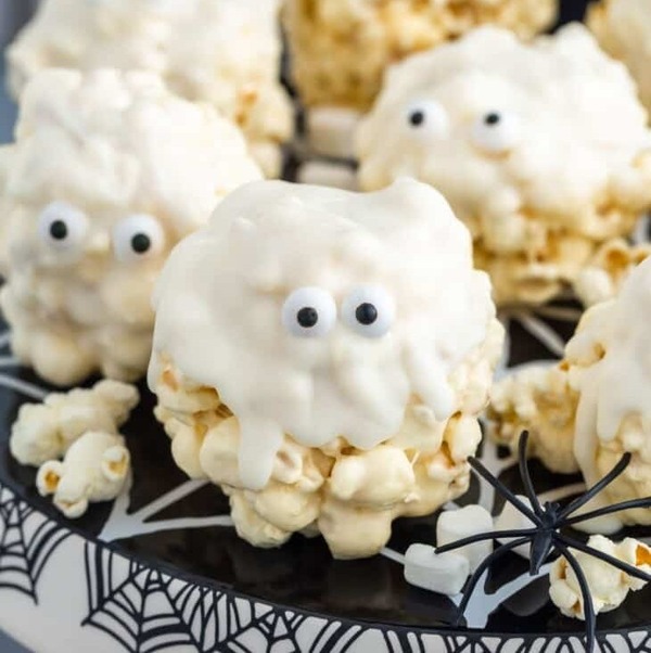 “Ghost marshmallow popcorn balls dipped in white candy melts and decorated with candy eyes for a cute Halloween treat kids can help make