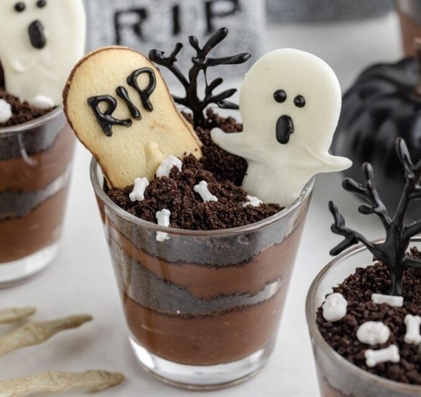 Halloween graveyard pudding cups made with chocolate pudding, crushed cookies for dirt, and decorated with candy tombstones and ghosts.