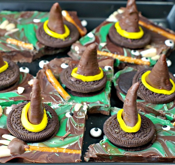 Easy melting witch Halloween chocolate bark made with swirled milk and dark chocolate, green candy melts, and decorated with candy witch hats and brooms for a spooky party treat.