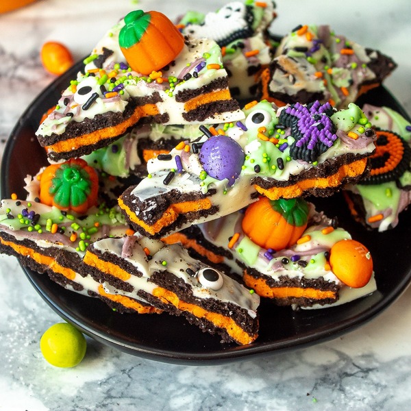 Halloween candy bark layered with white chocolate, Halloween Oreos, candy pumpkins, M&Ms, and sprinkles for an easy party-ready treat.