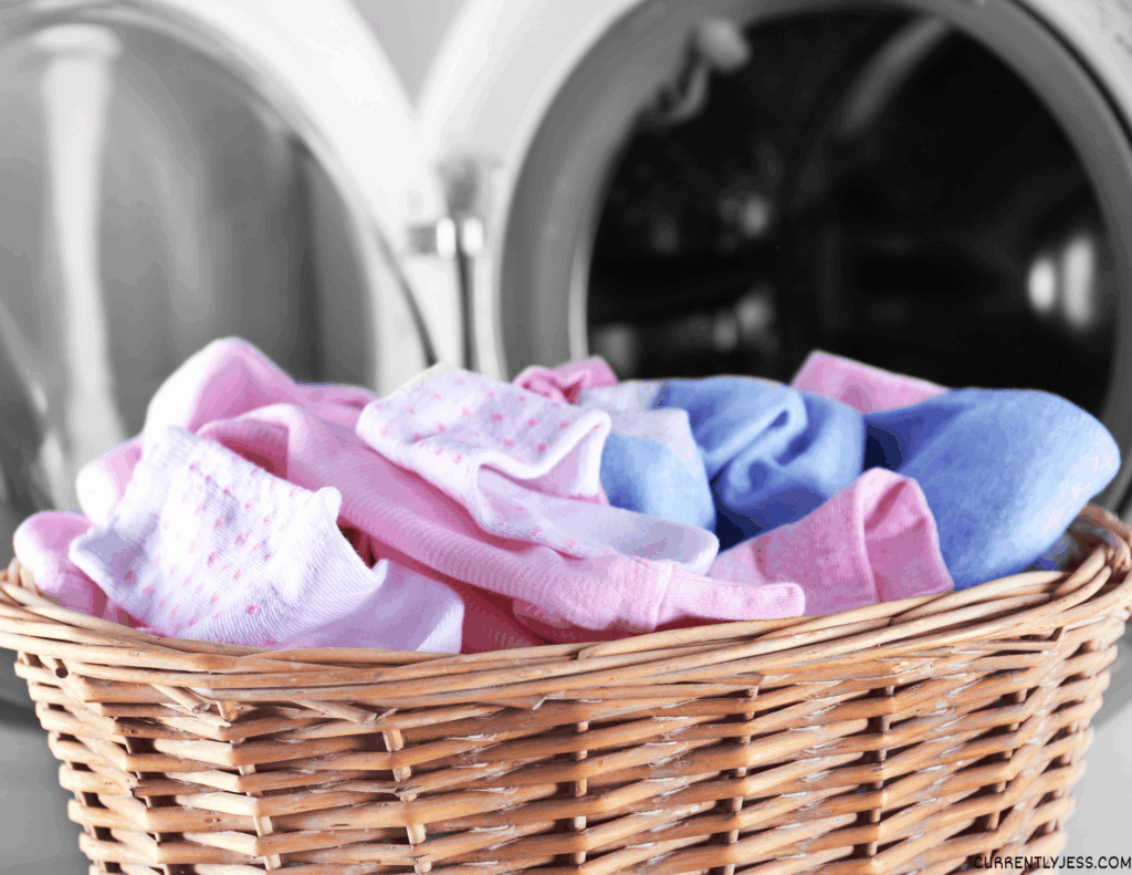 Stack of baby clothes sitting in front of a washing machine, showing how caring for clothes can help save money.