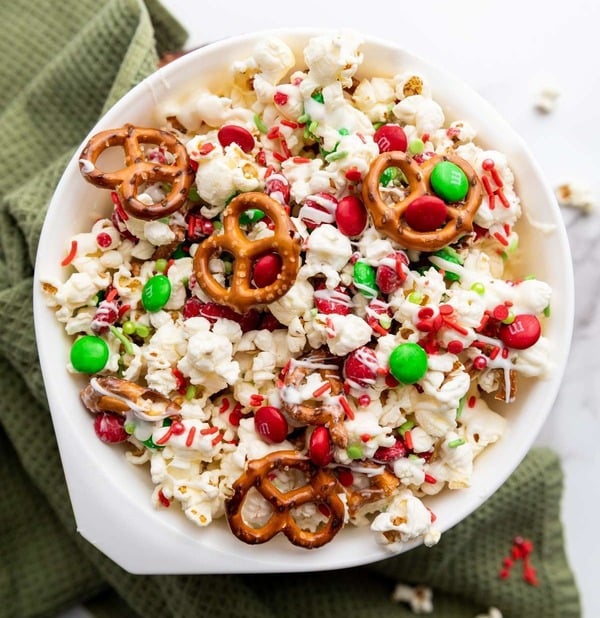 Christmas popcorn mix with pretzels, red and green M&Ms, sprinkles, and white chocolate drizzle, a fun holiday snack for kids.