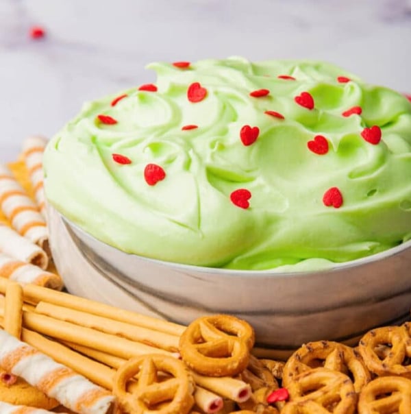 Grinch dip made with cream cheese, whipped topping, and green food coloring topped with red heart sprinkles, an easy no-bake Christmas dessert dip for kids.