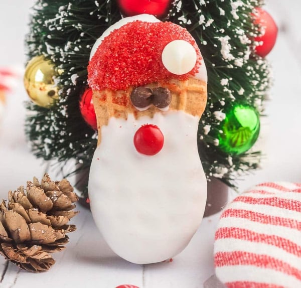 Santa Nutter Butter cookies decorated with red sugar sprinkles, white candy coating, candy eyes, and mini marshmallows, an easy no-bake Christmas cookie for kids.