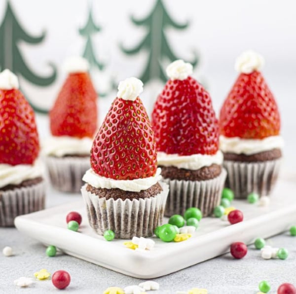 Chocolate orange Christmas muffins topped with cream cheese frosting and strawberry Santa hats, a festive holiday treat for kids and families.