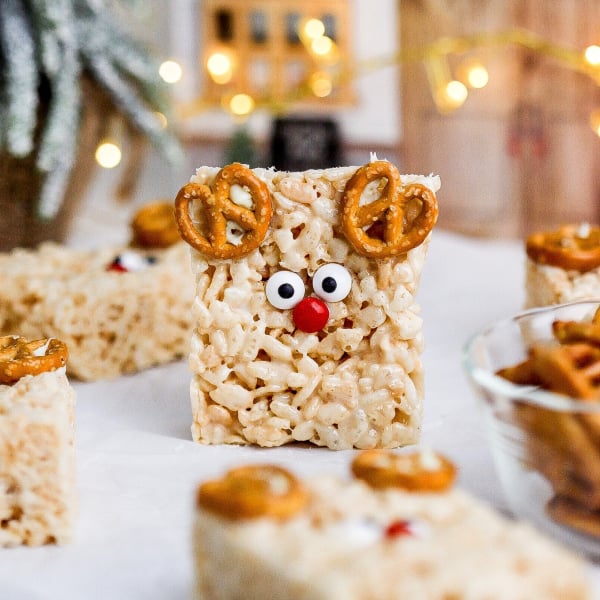 Reindeer Rice Krispie treats decorated with pretzel antlers, candy eyes, and red M&M noses, a fun no-bake Christmas dessert for kids.